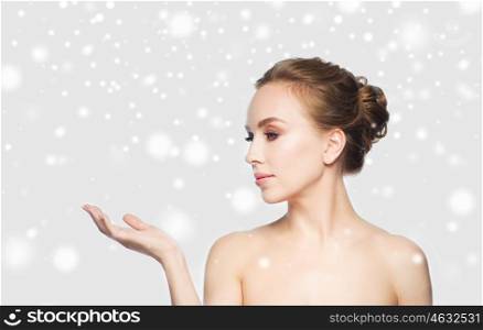 beauty, people, advertisement, winter and health concept - beautiful young woman holding something on palm of her hand over gray background and snow