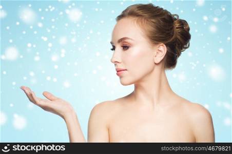 beauty, people, advertisement, winter and health concept - young woman holding something on palm of her hand over blue background and snow