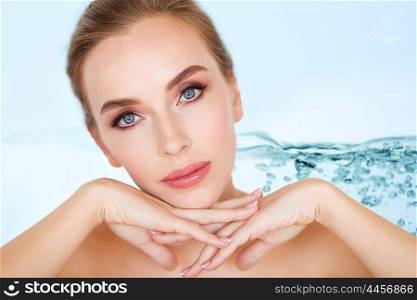 beauty, people and body care concept -beautiful young woman face and hands over water splash bubbles on blue background
