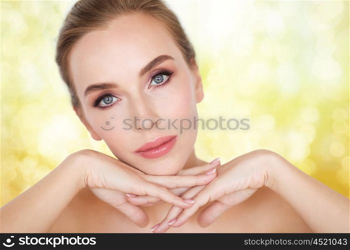 beauty, people and body care concept -beautiful young woman face and hands over yellow holidays lights background