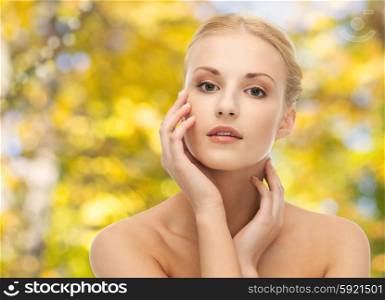 beauty, people and body care concept - beautiful young woman touching her face over yellow autumn background