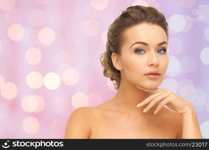 beauty, people and body care concept - beautiful young woman touching her face over pink background