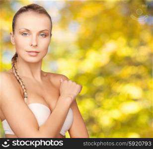beauty, people and body care concept - beautiful young woman with bare shoulders over yellow autumn background