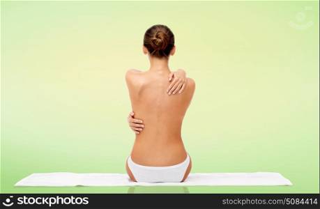 beauty, people and bodycare concept - beautiful topless young woman in white panties sitting on towel from back over green natural background. beautiful topless young woman on towel from back. beautiful topless young woman on towel from back