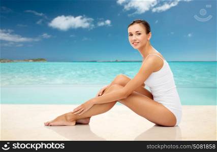 beauty, people and bodycare concept - beautiful woman in white underwear touching her smooth bare legs over exotic tropical beach background. beautiful woman touching her legs on summer beach