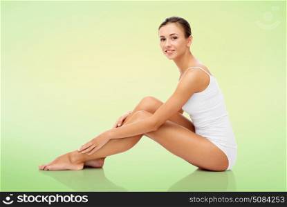 beauty, people and bodycare concept - beautiful woman in white underwear touching her smooth bare legs over green natural background. beautiful woman touching her smooth bare legs. beautiful woman touching her smooth bare legs
