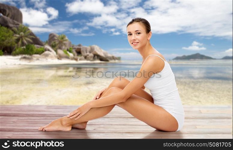 beauty, people and bodycare concept - beautiful woman touching her smooth bare legs over exotic beach background. beautiful woman touching her bare legs on beach