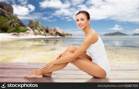 beauty, people and bodycare concept - beautiful woman touching her smooth bare legs over exotic beach background. beautiful woman touching her bare legs on beach