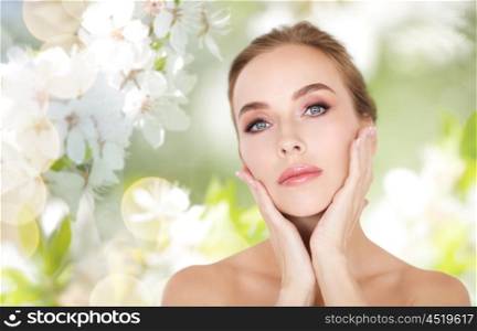 beauty, people and bodycare concept -beautiful young woman face and hands over natural spring cherry blossom background