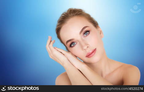 beauty, people and bodycare concept -beautiful young woman face and hands over blue background