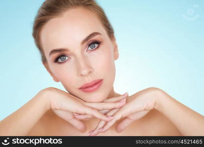 beauty, people and bodycare concept -beautiful young woman face and hands over blue background