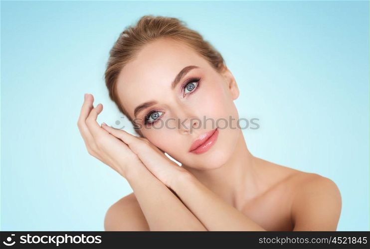beauty, people and bodycare concept -beautiful young woman face and hands over blue background