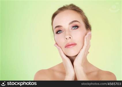 beauty, people and bodycare concept -beautiful young woman face and hands over green background