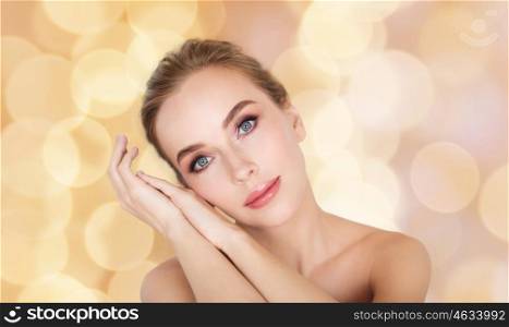 beauty, people and bodycare concept - beautiful young woman face and hands over holidays lights background