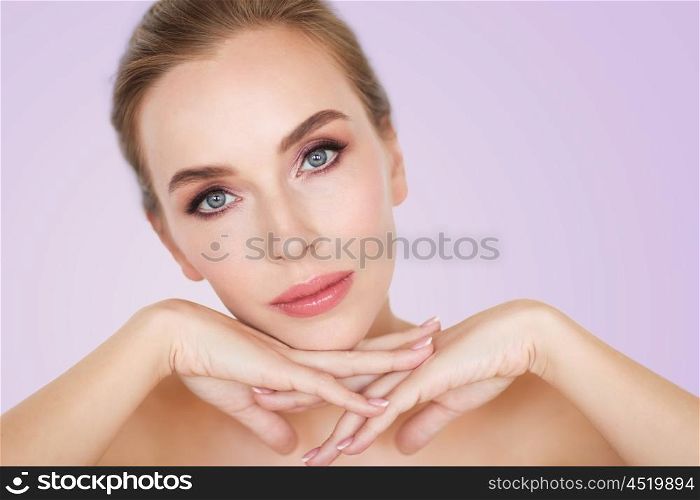 beauty, people and bodycare concept -beautiful young woman face and hands over violet background