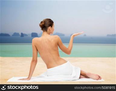 beauty, people and bodycare concept - beautiful young woman in white towel with bare top holding something invisible over infinity edge pool background. beautiful young woman in white towel with bare top