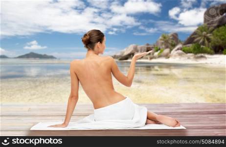 beauty, people and bodycare concept - beautiful young woman in white towel with bare top holding something invisible over exotic beach background. beautiful woman in towel with bare top on beach. beautiful woman in towel with bare top on beach