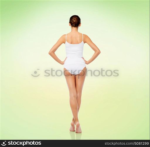 beauty, people and bodycare concept - beautiful young woman in white underwear from back over green background. beautiful young woman in white underwear