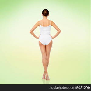 beauty, people and bodycare concept - beautiful young woman in white underwear from back over green background. beautiful young woman in white underwear