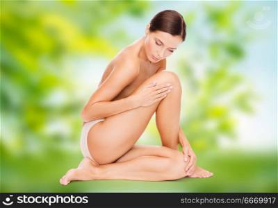 beauty, people and bodycare concept - beautiful young woman touching her leg over green natural background. beautiful young woman touching her leg. beautiful young woman touching her leg
