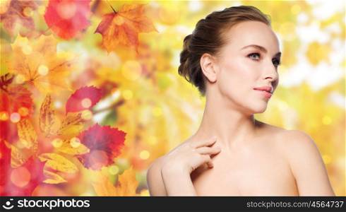 beauty, people and bodycare concept - beautiful young woman touching her neck over natural autumn leaves and lights background