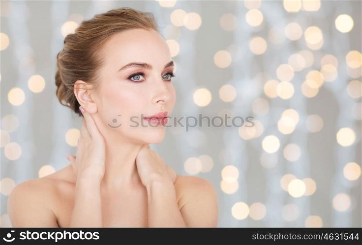 beauty, people and bodycare concept - beautiful young woman touching her neck over holidays lights background