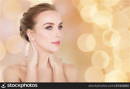 beauty, people and bodycare concept - beautiful young woman touching her neck over holidays lights background