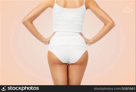 beauty, people and bodycare concept - close up of beautiful young woman body in white underwear from back over beige background. close up of woman body in white underwear