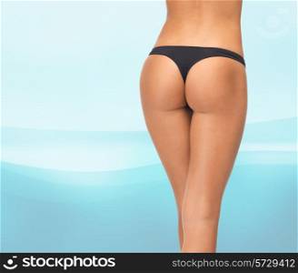 beauty, people and bodycare concept - close up of female legs in black bikini panties over blue waves background