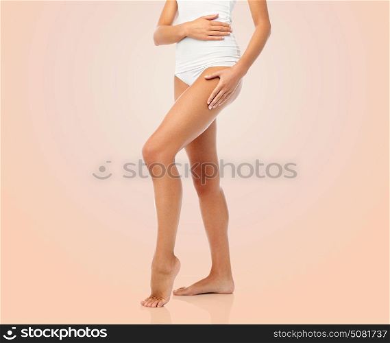 beauty, people and bodycare concept - legs of beautiful young woman in white underwear over beige background. legs of beautiful young woman in white underwear