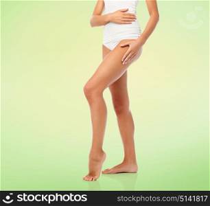 beauty, people and bodycare concept - legs of beautiful young woman in white underwear over green natural background. legs of beautiful young woman in white underwear