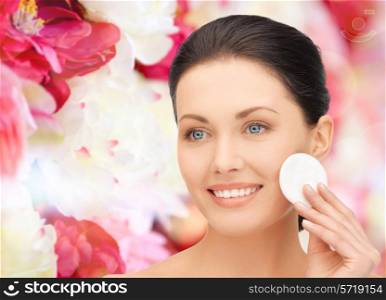 beauty, people and health concept - beautiful smiling woman cleaning face skin with cotton pad over pink floral background