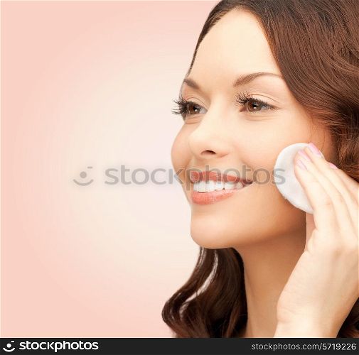 beauty, people and health concept - beautiful smiling woman cleaning face skin with cotton pad over pink background