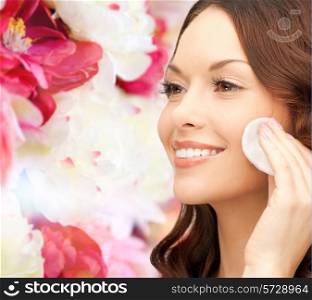 beauty, people and health concept - beautiful smiling woman cleaning face skin with cotton pad over pink floral background