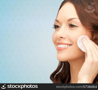 beauty, people and health concept - beautiful smiling woman cleaning face skin with cotton pad over blue background