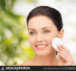 beauty, people and health concept - beautiful smiling woman cleaning face skin with cotton pad over green background
