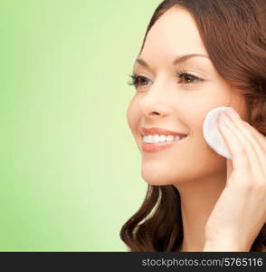 beauty, people and health concept - beautiful smiling woman cleaning face skin with cotton pad over green background