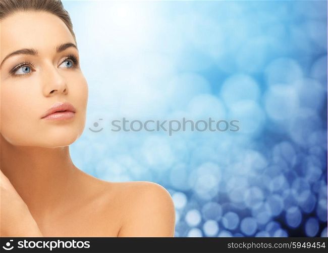 beauty, people and health concept - beautiful young woman face and bare shoulder over blue lights background