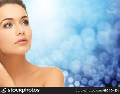 beauty, people and health concept - beautiful young woman face and bare shoulder over blue lights background