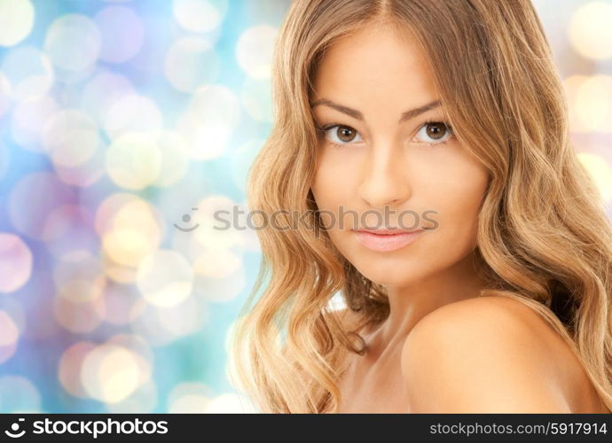 beauty, people and health concept - beautiful young woman face over blue holidays lights background