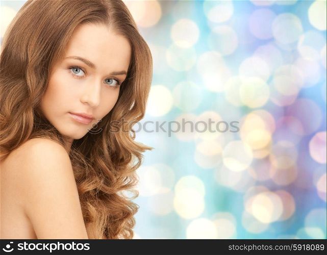 beauty, people and health concept - beautiful young woman face over blue holidays lights background