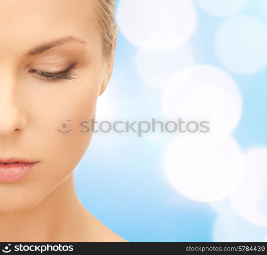 beauty, people and health concept - beautiful young woman face over blue lights background