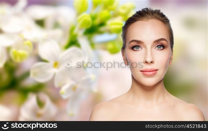 beauty, people and health concept - beautiful young woman face over natural lilac blossom background
