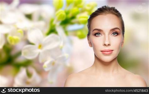 beauty, people and health concept - beautiful young woman face over natural lilac blossom background