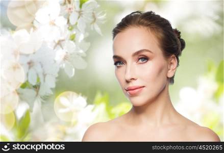 beauty, people and health concept - beautiful young woman face over natural spring cherry blossom background