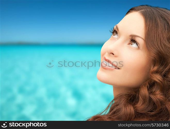 beauty, people and health concept - beautiful young woman looking up over blue sky and sea background