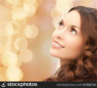 beauty, people and health concept - beautiful young woman looking up over beige lights background