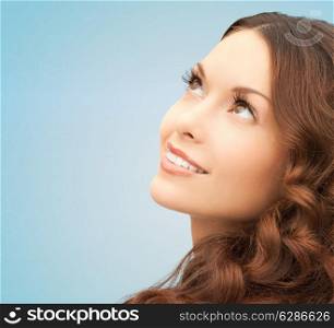 beauty, people and health concept - beautiful young woman looking up over blue background