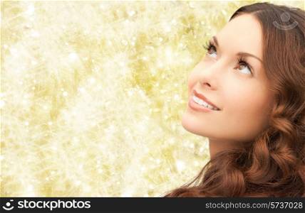 beauty, people and health concept - beautiful young woman looking up over yellow lights background