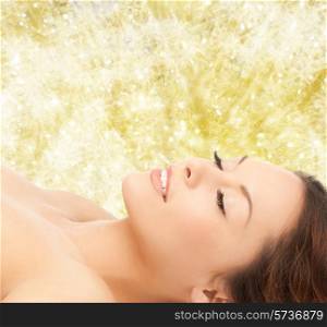 beauty, people and health concept - beautiful young woman lying with closed eyes over yellow lights background